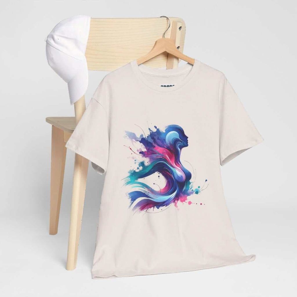 Ice grey cotton t-shirt with colorful abstract graphic print draped on wooden chair next to a white baseball cap