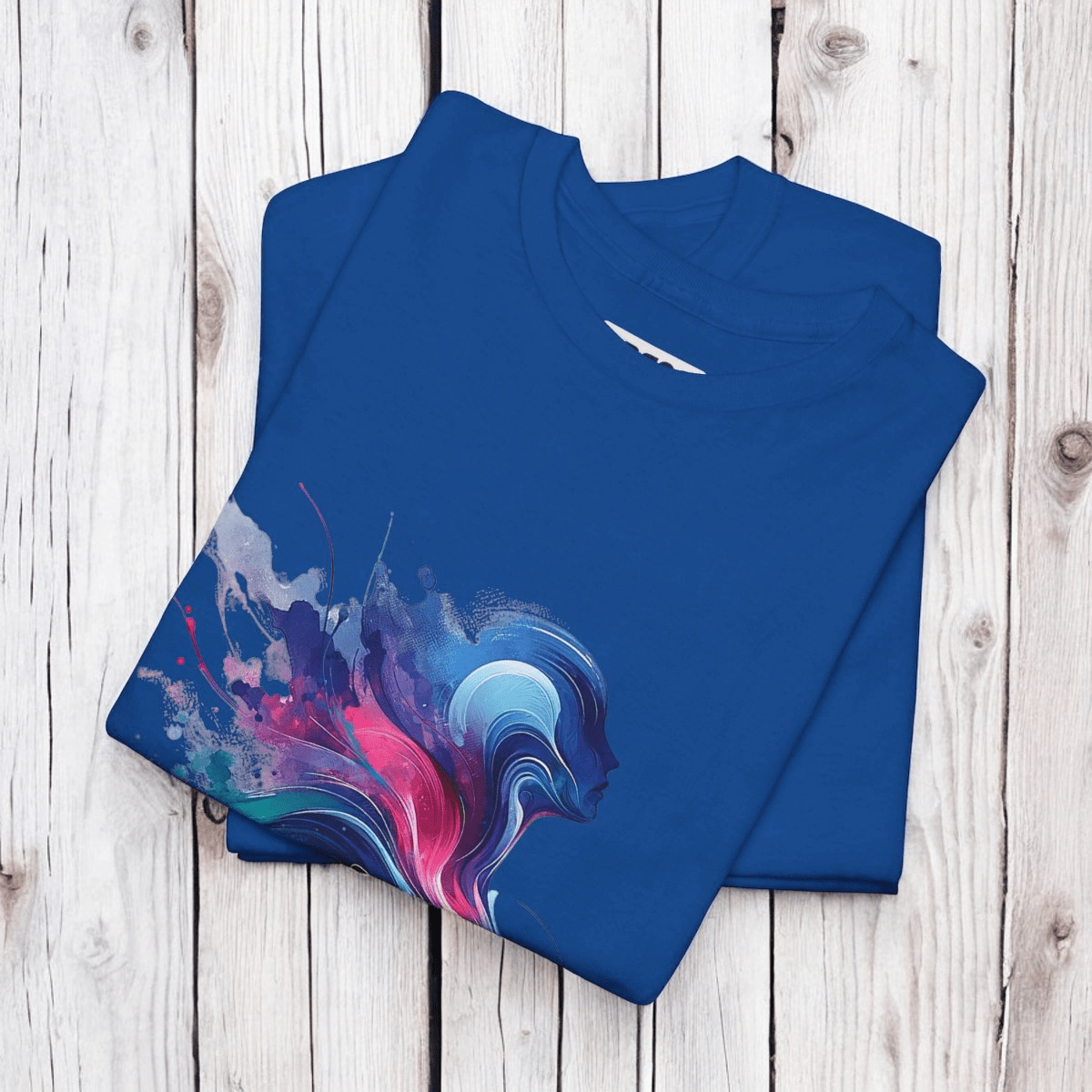 Blue cotton T-shirt with crew neck and multicolor abstract splash design laid flat on a wooden surface
