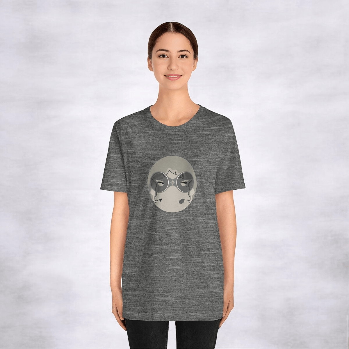Woman in gray tee featuring circular, stylized face design with abstract mountain, moon elements, white backdrop