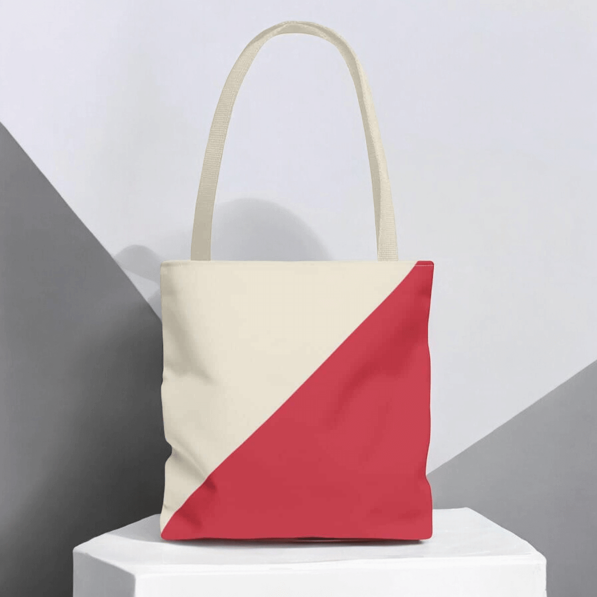 Cream and red tote bag with diagonal design with beige handles on a minimalist gray geometric background