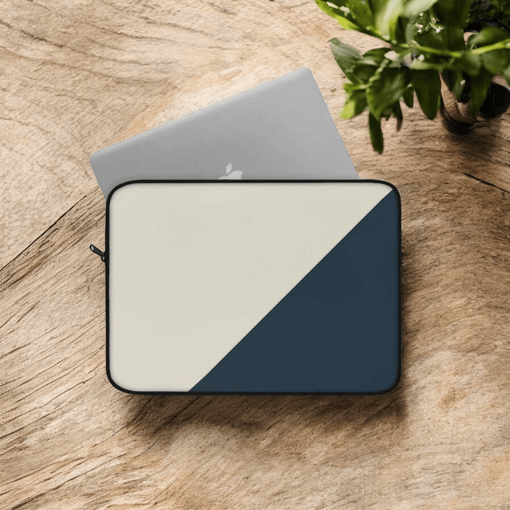 Laptop sleeve in beige and dark grey canvas with a diagonal color block design placed on wooden surface near plant