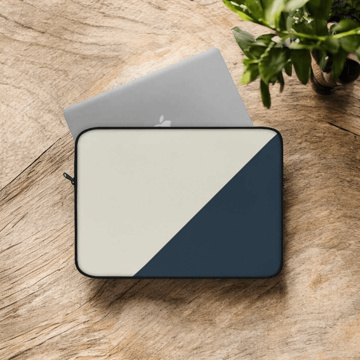 Laptop sleeve in beige and dark grey canvas with a diagonal color block design placed on wooden surface near plant