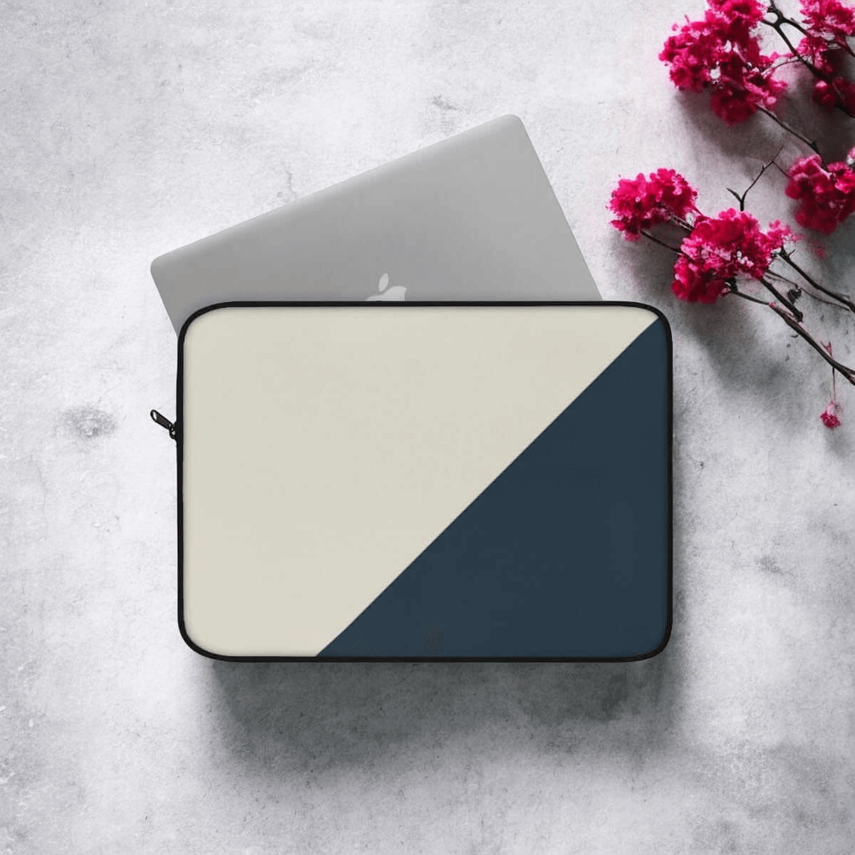 Laptop sleeve in beige and navy fabric with minimalist design, laid on concrete with scattered pink flowers