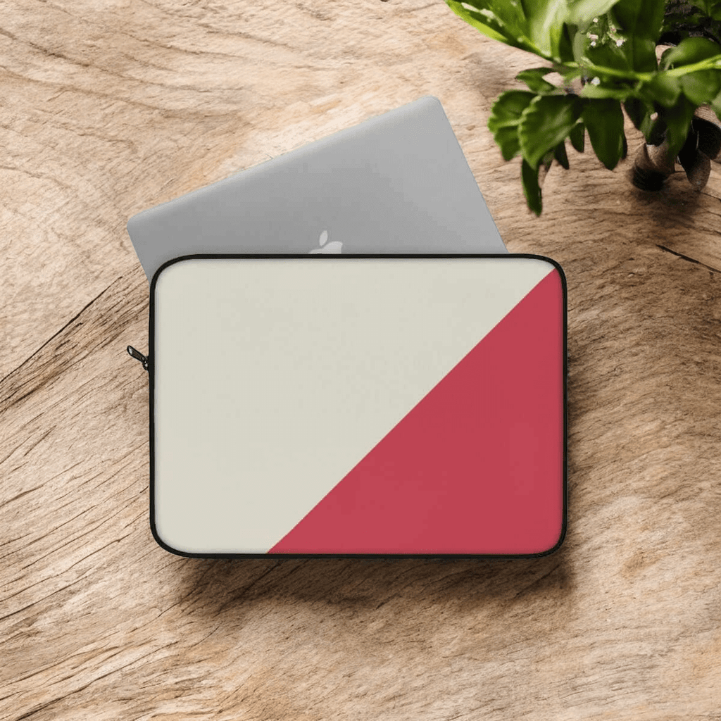 Laptop sleeve with red and cream diagonal canvas design lying flat on wooden surface near green leafy plant
