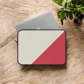 Laptop sleeve with red and cream diagonal canvas design lying flat on wooden surface near green leafy plant