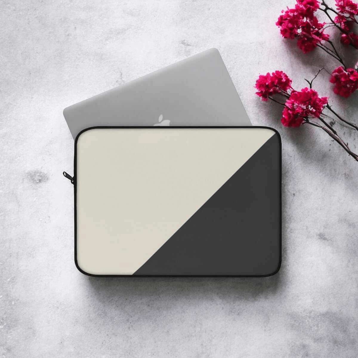 Laptop in slim dark grey fabric case with zipper closure resting on marble surface next to red flowers