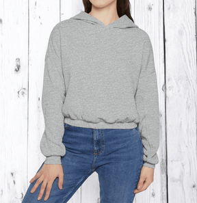 Gray fleece hoodie with kangaroo pocket and ribbed cuffs worn by person standing against white wooden wall