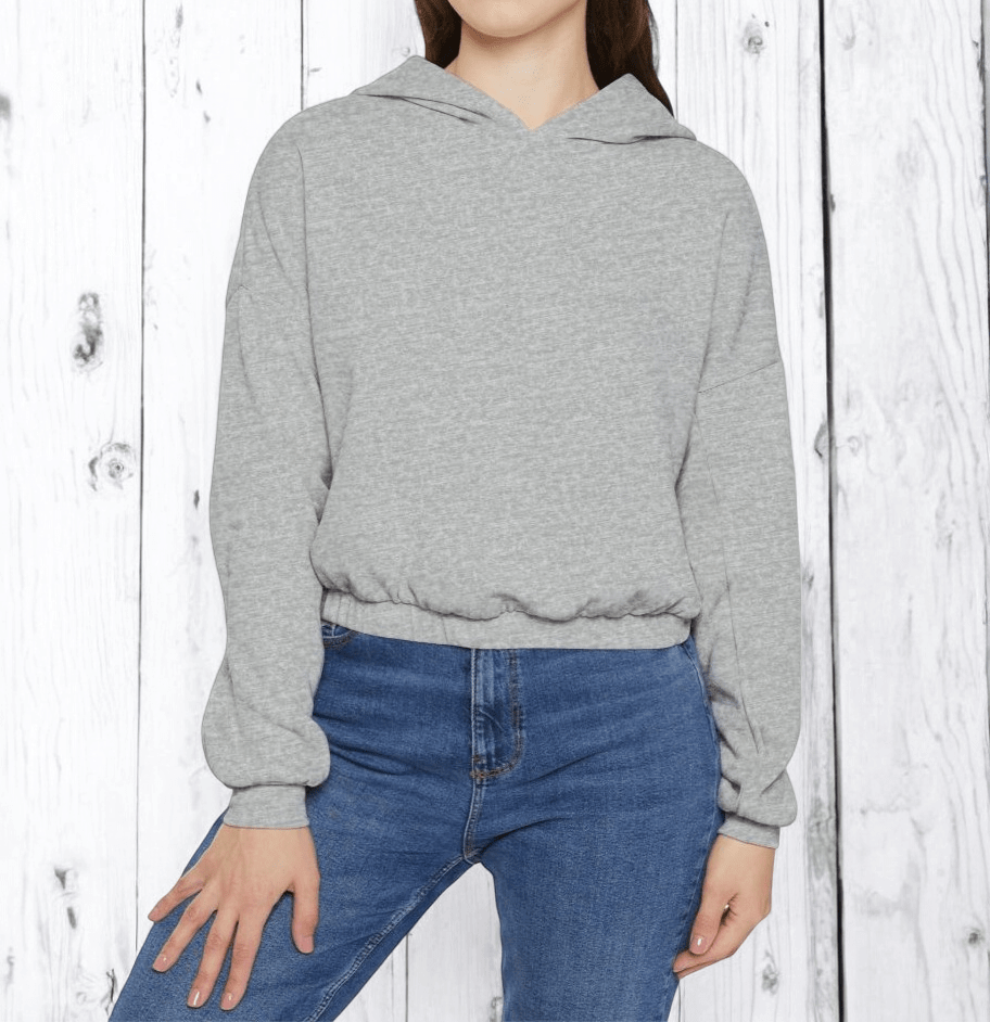 Gray fleece hoodie with kangaroo pocket and ribbed cuffs worn by person standing against white wooden wall