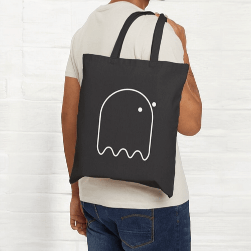 Black canvas tote bag with white ghost graphic, casual design and dual top handles against neutral background