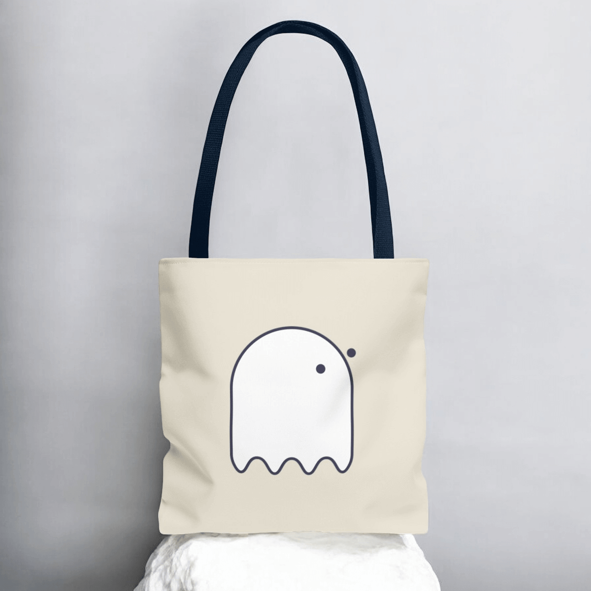 Navy blue fabric tote bag with button-eyed ghost graphic on front in white print and two handles