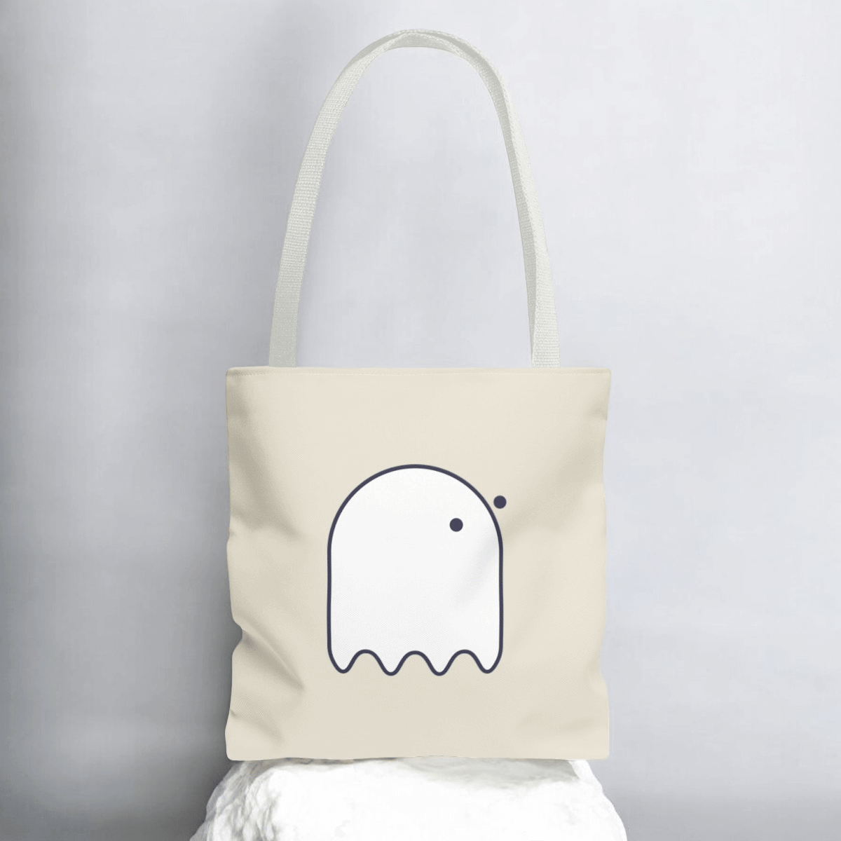 White cotton tote bag with button-eyed ghost patch on front center and flat handles for carrying