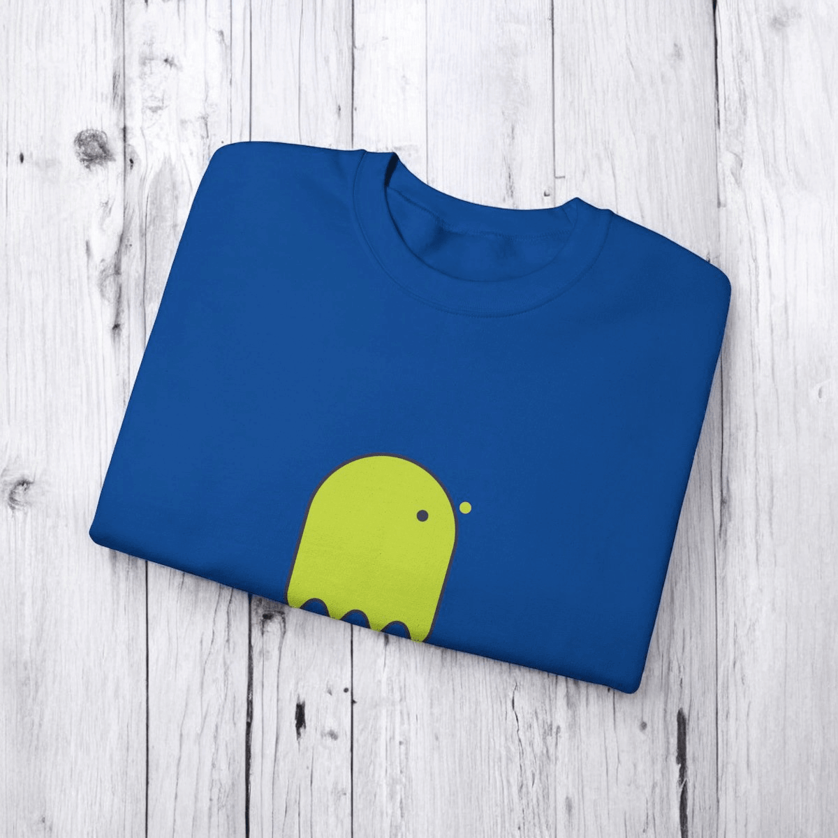 Blue cotton t-shirt featuring a green abstract creature graphic on the chest, laid flat on a wooden surface
