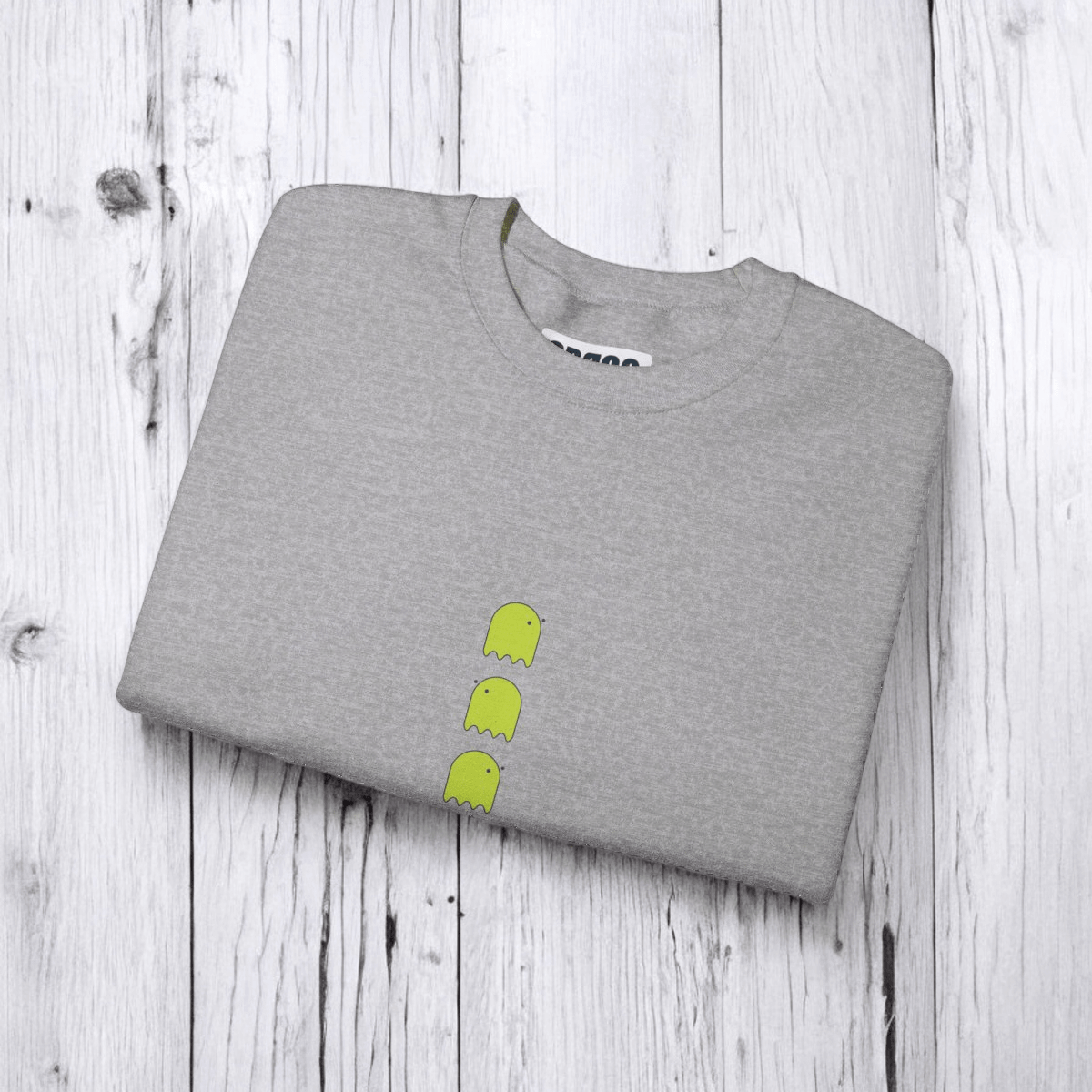 Gray cotton t-shirt folded neatly with three small lime green ghost graphics on front, displayed on wooden surface