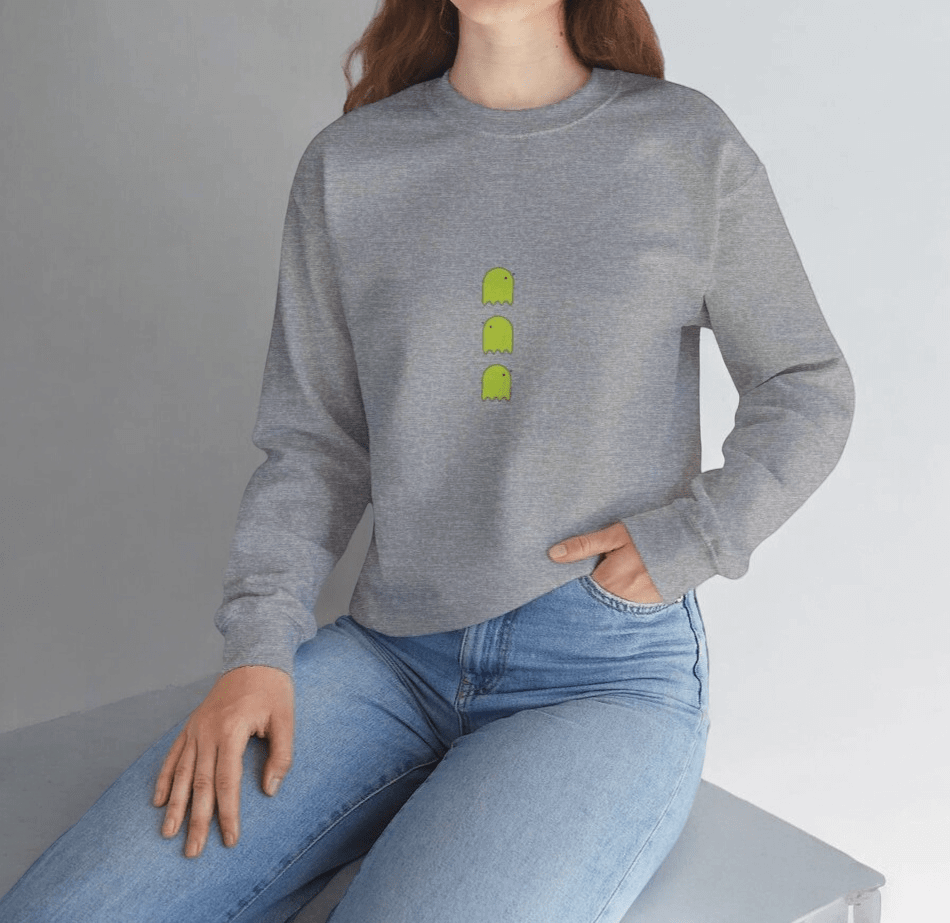Gray knit sweater with green cartoon ghost design, crew neck, and ribbed cuffs worn with blue denim jeans