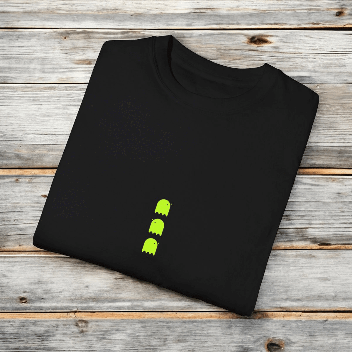 Black cotton T-shirt with neon green ghost graphics in a retro arcade design laid flat on wooden surface