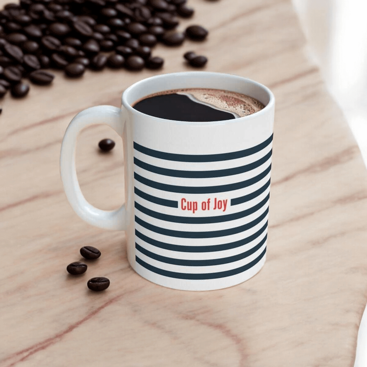 Ceramic white mug with black horizontal stripes and 'Cup of Joy' text, filled with coffee and surrounded by coffee beans