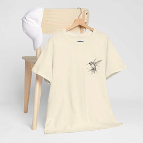Beige cotton T-shirt with minimalist bird graphic draped on a chair beside a white baseball cap