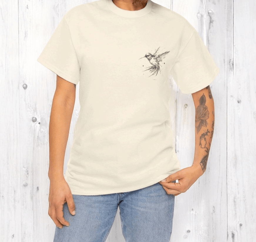 Cream cotton t-shirt with artistic hummingbird illustration, worn with light blue jeans and visible arm tattoos
