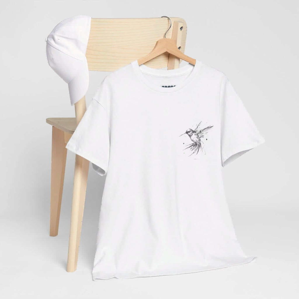 White cotton t-shirt with minimalist bird graphic and plain white cap displayed on a wooden chair with neutral background