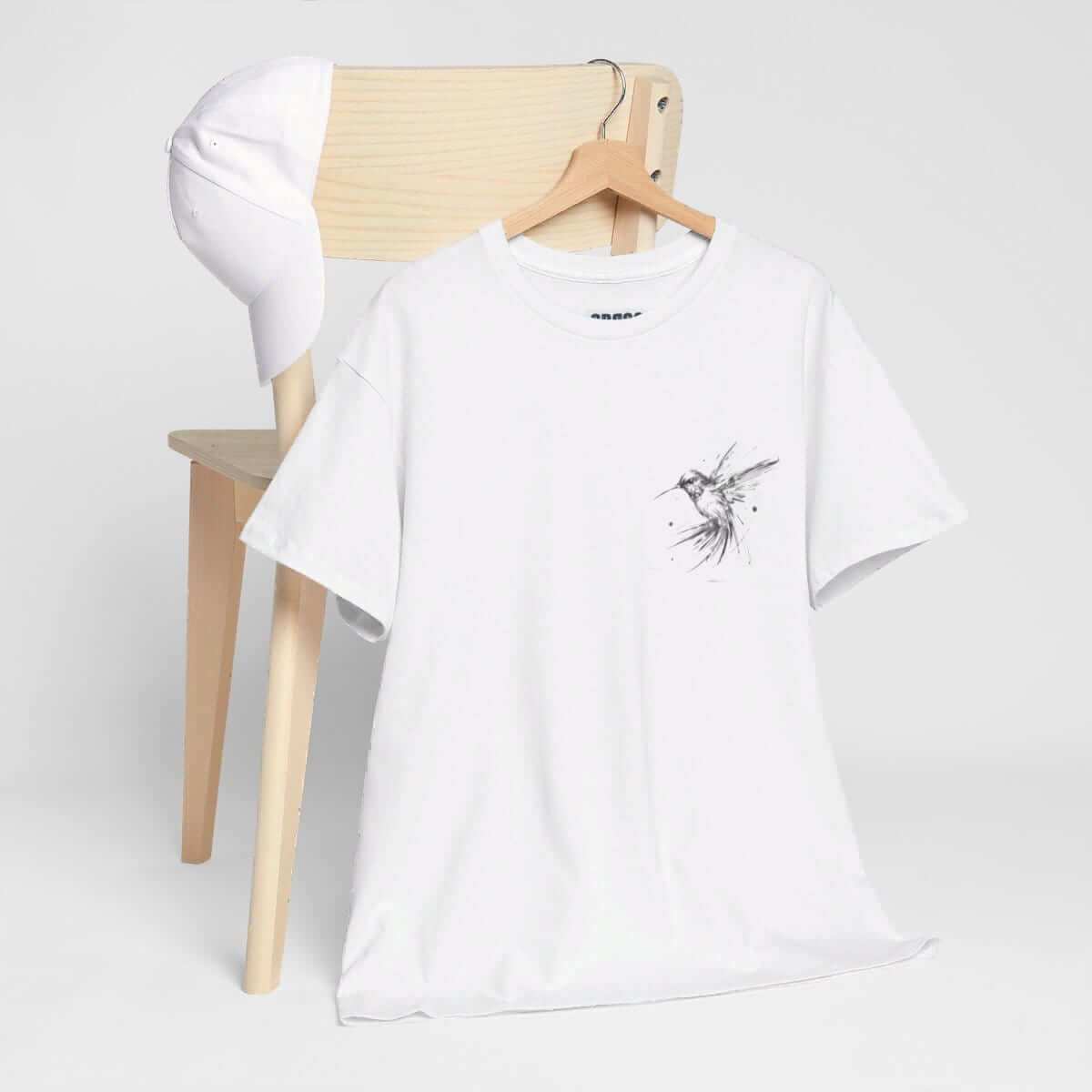 White cotton t-shirt with minimalist bird graphic and plain white cap displayed on a wooden chair with neutral background