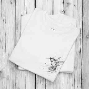 White cotton T-shirt with black hummingbird sketch printed on front, laid flat on a rustic wooden surface