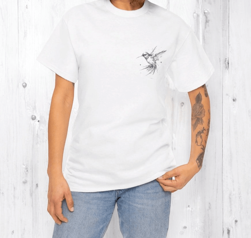 White cotton t-shirt with black bird graphic design worn with blue jeans, shown on tattooed person in casual setting