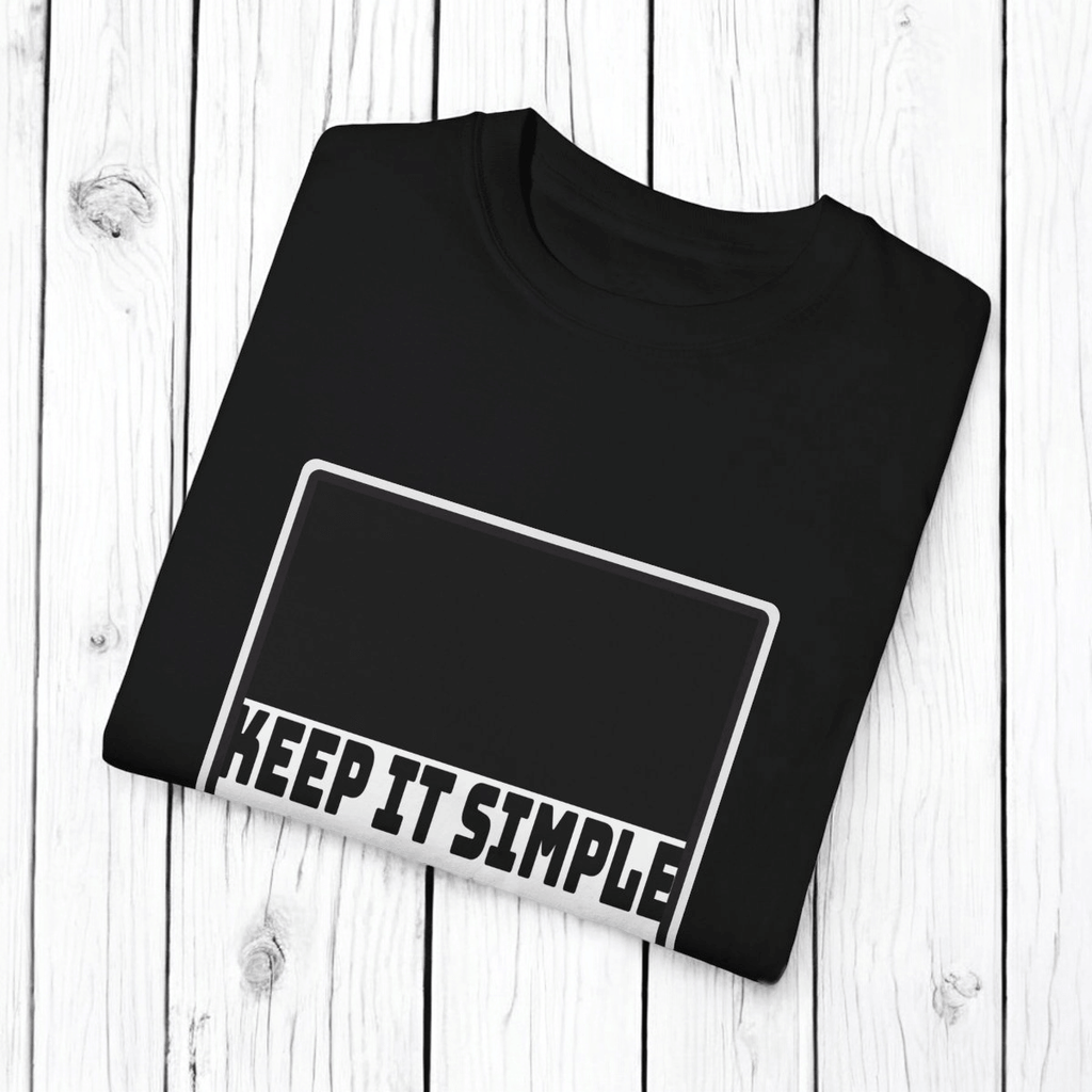 Black cotton T-shirt with bold white sans-serif text reading KEEP IT SIMPLE displayed flat on a wooden surface