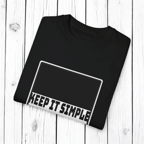 Black cotton T-shirt with bold white sans-serif text reading KEEP IT SIMPLE displayed flat on a wooden surface