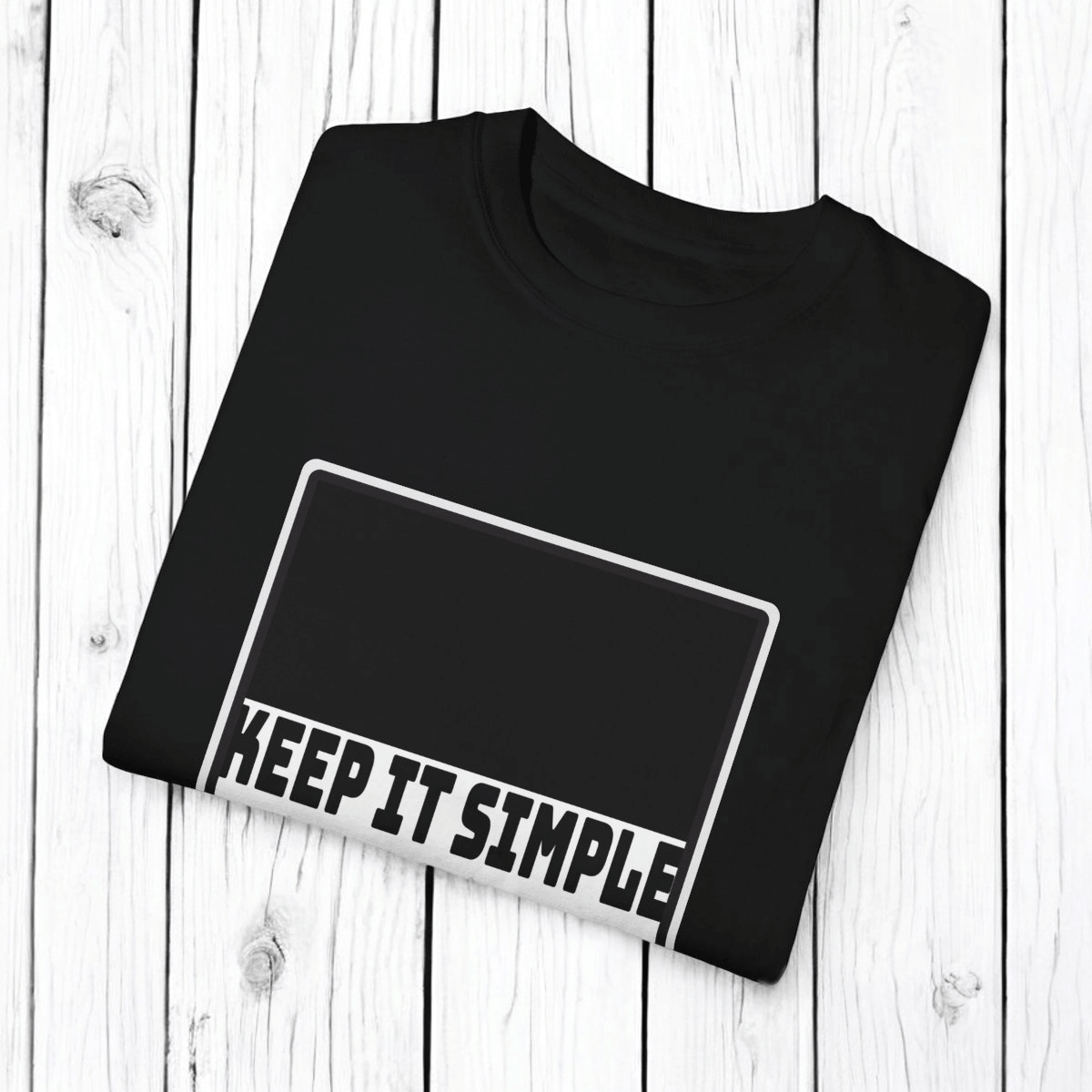 Black cotton T-shirt with bold white sans-serif text reading KEEP IT SIMPLE displayed flat on a wooden surface
