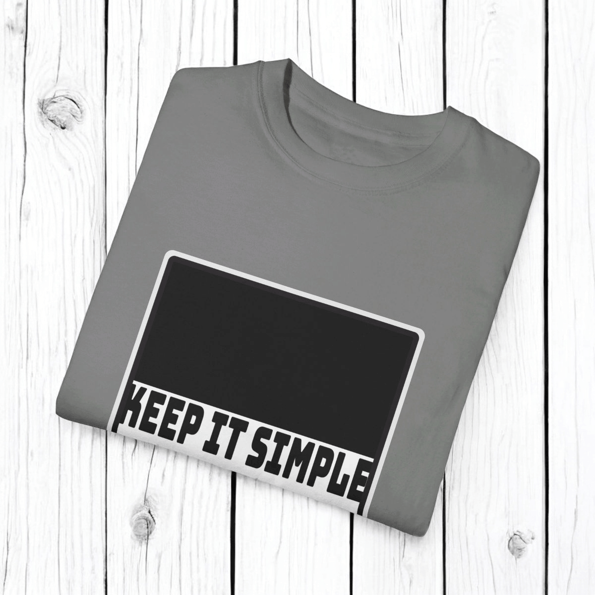 Grey cotton T-shirt with round neckline and bold KEEP IT SIMPLE text neatly folded on a wooden surface