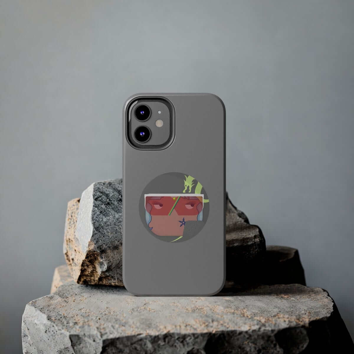 Gray plastic phone case for iPhone 15 featuring colorful abstract face graphic laying on textured rocky surface