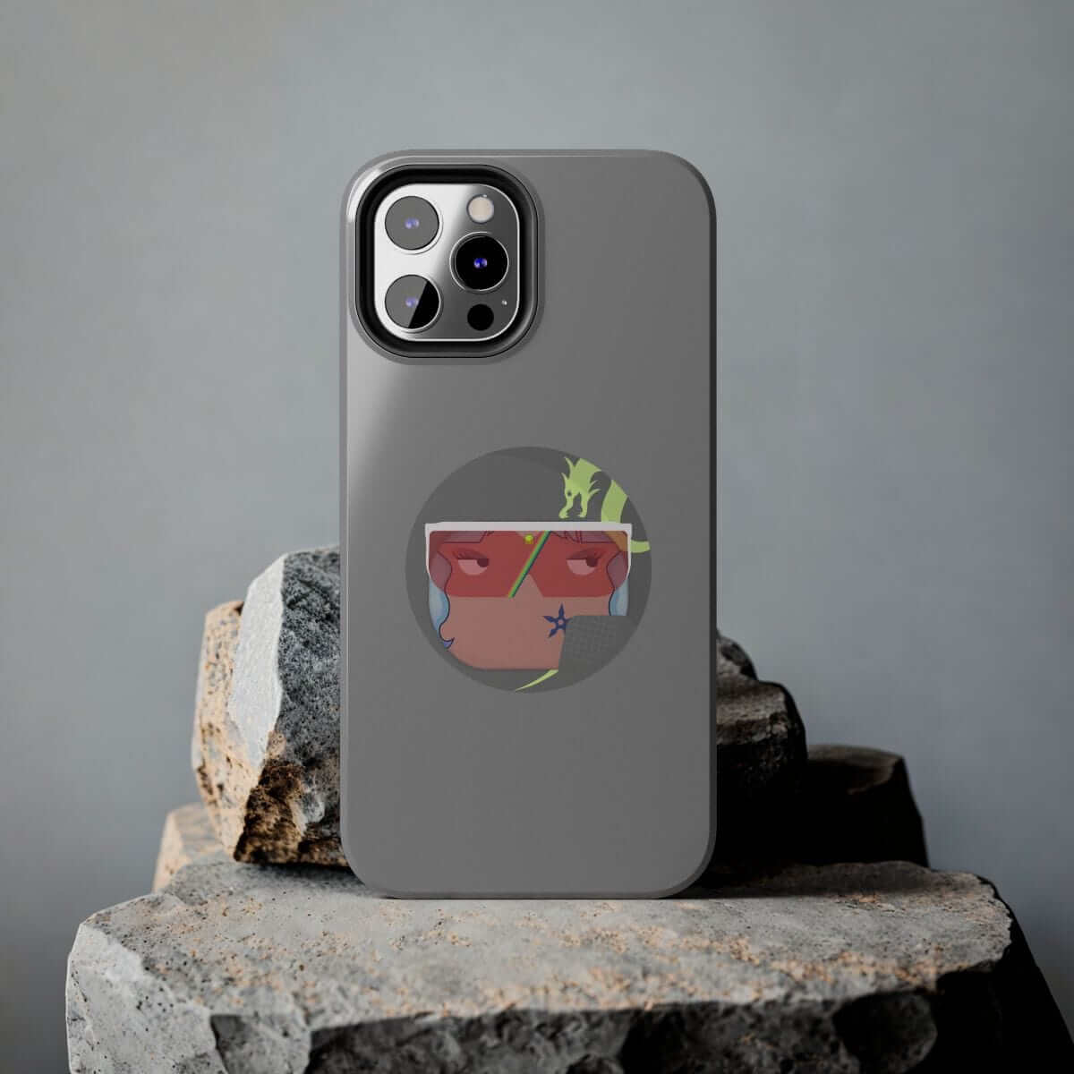 Dark gray matte phone case for iPhone 15 Pro with cartoon-style illustrated character, displayed on large textured rocks